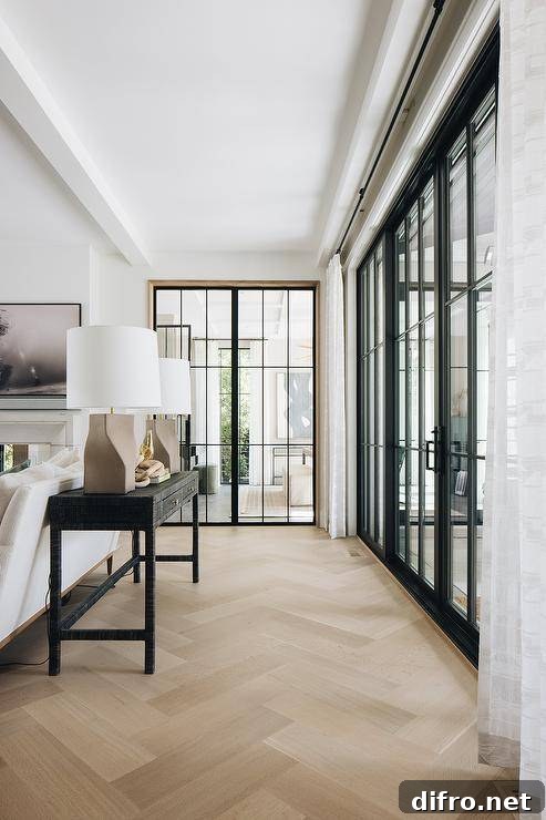 Taupe lamps are placed atop a black console table positioned on a herringbone floor behind a white sofa.