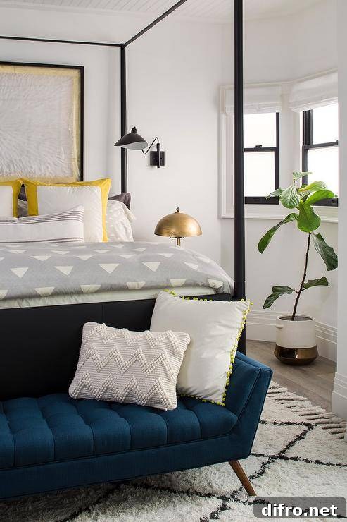 Blue mid century modern bench sits on a Moroccan wool rug in front of a black canopy bed accented with gray and white bedding.