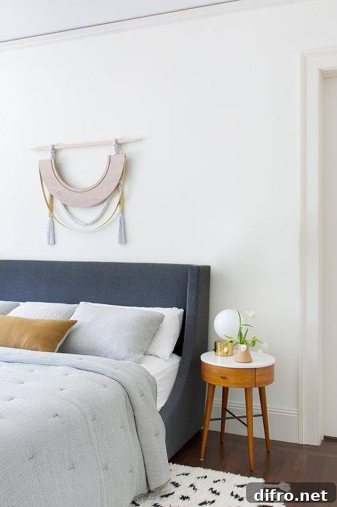 Light gray quilt on a dark gray upholstered bed in a transitional bedroom accented with a Moroccan rug and a round mid century modern bedside table.