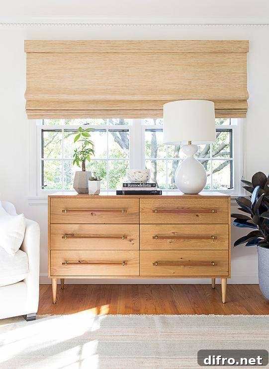A stunning Aerin Gannet Table Lamp sits atop a mid-century modern dresser placed beneath a bedroom window covered in a bamboo roman shade.