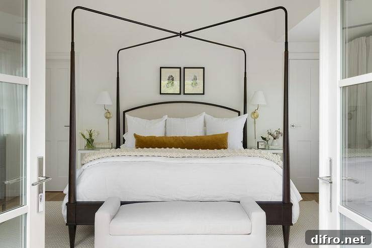 A white settee is positioned at the foot of a gray and black canopy bed draped with an ivory knitted throw blanket and a burnt orange velvet lumbar pillow.