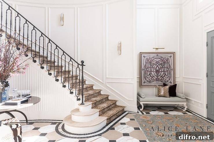 Grand curved staircase with iron railing and patterned runner.