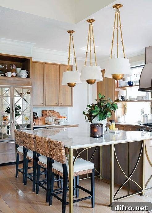 A brown wood island with brass legs is accented with a striped marble countertop seating four brown woven stools facing a sink wiht a polished nickel gooseneck faucet lit by three white and gold pendants.