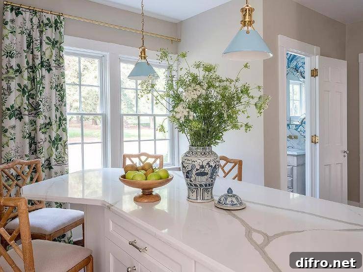 Vintage blue lanterns light a white angled kitchen island topped with a marble-look countertop and paired with tan bamboo counter stools. Windows are covered in white and green botanical curtains.
