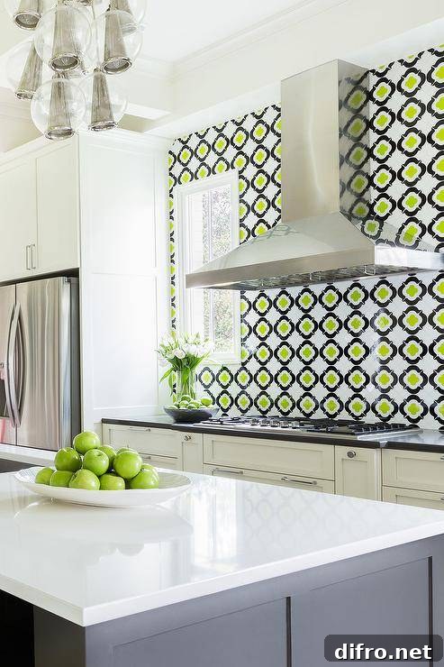 White and gray kitchen features white perimeter cabinets paired with black quartz countertops and a black and green quatrefoil tile backsplash, Galeria Marble Mosaics Quatrefoil Glass. A stainless steel kitchen hood stands over an integrated gas cooktop flanked by pull out spice racks below. An Arteriors Caviar Adjustable Cluster Pendant illuminates a gray kitchen island topped with white quartz.