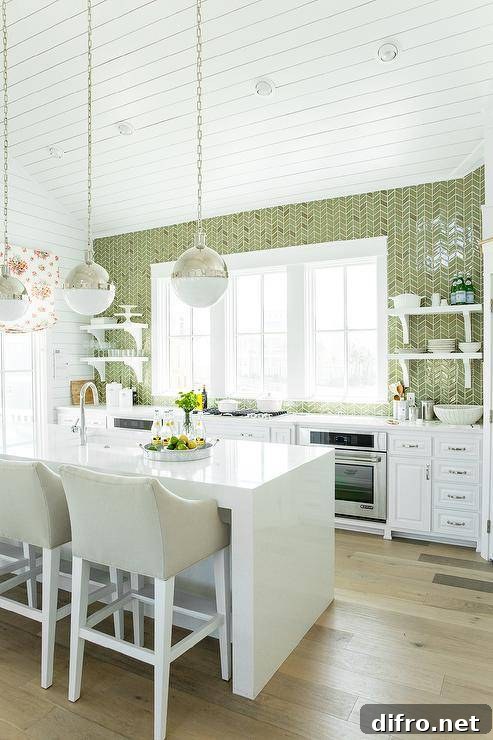 White and green kitchen features white cabinets paired with white quartz countertops and a ceiling height green herringbone tiled backsplash. An integrated gas cooktop stands under windows flanked by stacked white shelves and oven to the left and stacked shelves and oven to the right. Two Hicks Pendants hang over a white quartz waterfall kitchen island fitted with a sink and gooseneck faucet lined with ivory swoop arm bar stools.