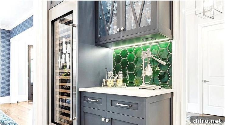 Contemporary home bar is fitted with blue cabinets donning polished nickel hardware and fixed against emerald green glass hexagon backsplash tiles under glass front mullion cabinets and beside a full size glass front wine fridge.