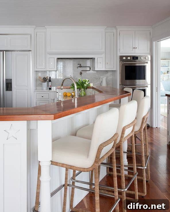 Ivory fabric and rope counter stools at a beadboard curved breakfast island in a cottage kitchen styled with a wood countertop complementing warm oak wood floors.