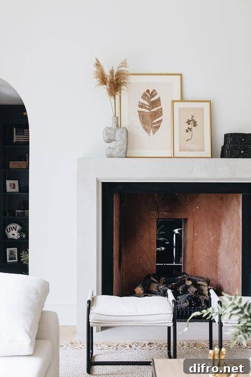 Black and white stools sit in front of a modern beveled fireplace mantel styled with botanical art in gold frames.