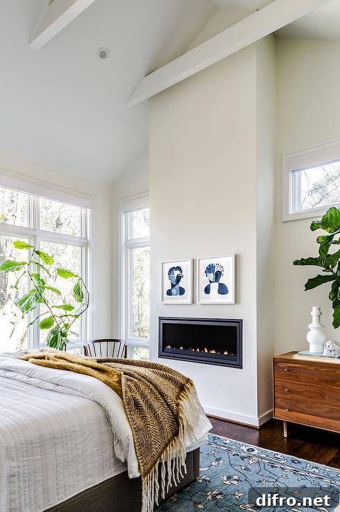 Restful bedroom boasts a gray bed placed on a blue floral rug facing a modern gas fireplace fitted beneath blue abstract art pieces.