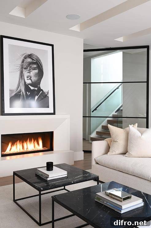 Living room features black and white art mounted over a modern beveled fireplace, an ivory sofa, and side-by-side black marble frame coffee tables.