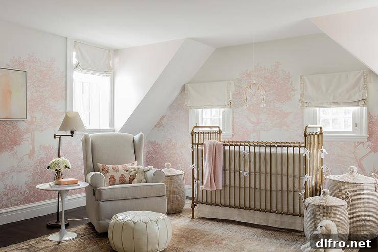 Nursing room with a gold metal crib and pink tree-themed wallpaper.