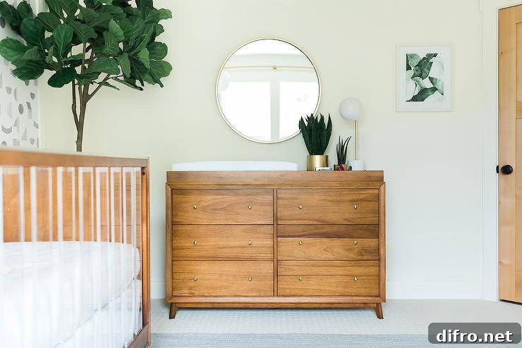 A round silver mirror hangs over a brown vintage dresser topped with a white changing pad.