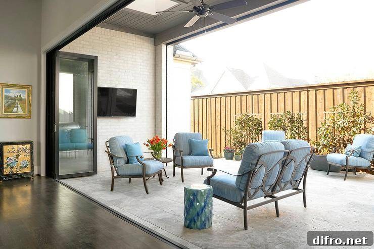 Outdoor patio design displaying glass and metal folding doors opening up to a travertine floor patio with blue seating and accents.