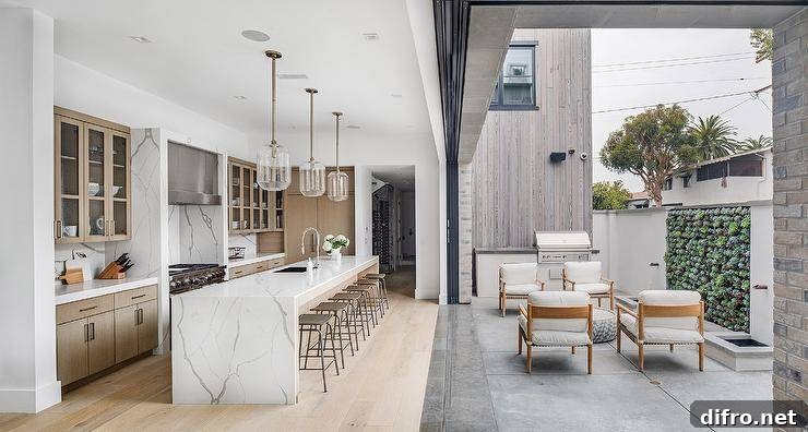 Golden teak chairs are placed on a patio on concrete pavers in front of sliding glass pocket doors that open to a kitchen.