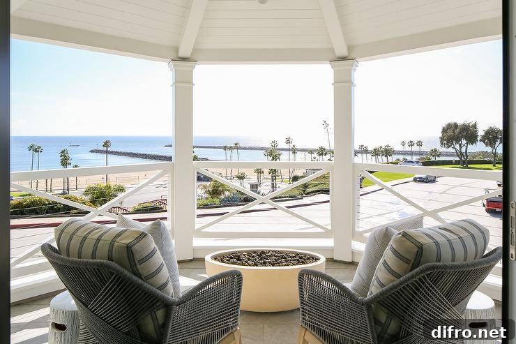 With a beautiful beach view, arm chairs sit on a bedroom balcony facing a round concrete fire pit.