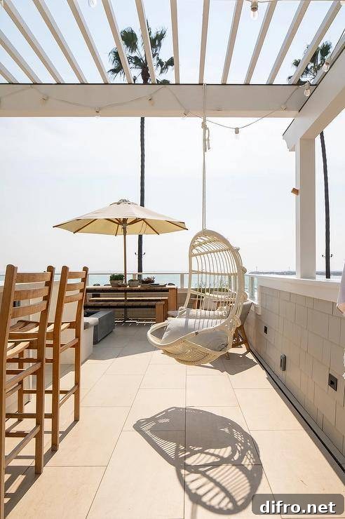 A beach cottage patio features a hanging white rattan chair hung from a white pergola.