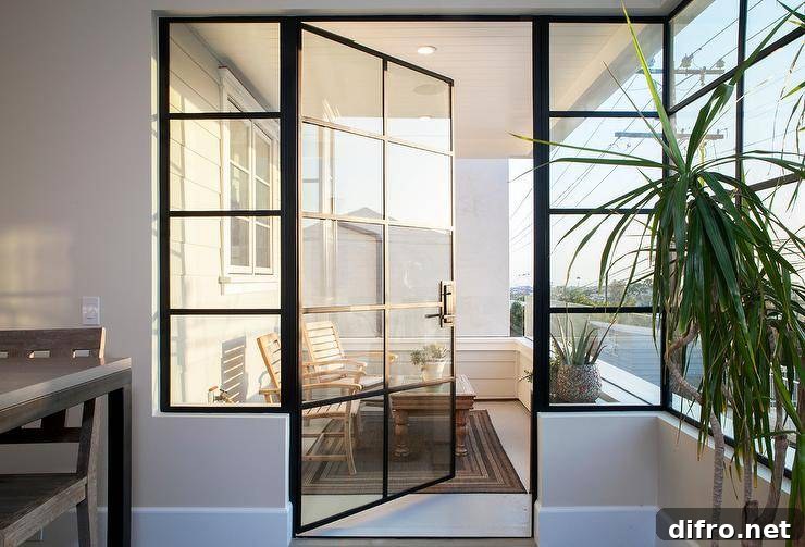 A glass and steel balcony door opens to a small balcony filled with teak chairs and coffee table atop a black bordered outdoor rug.