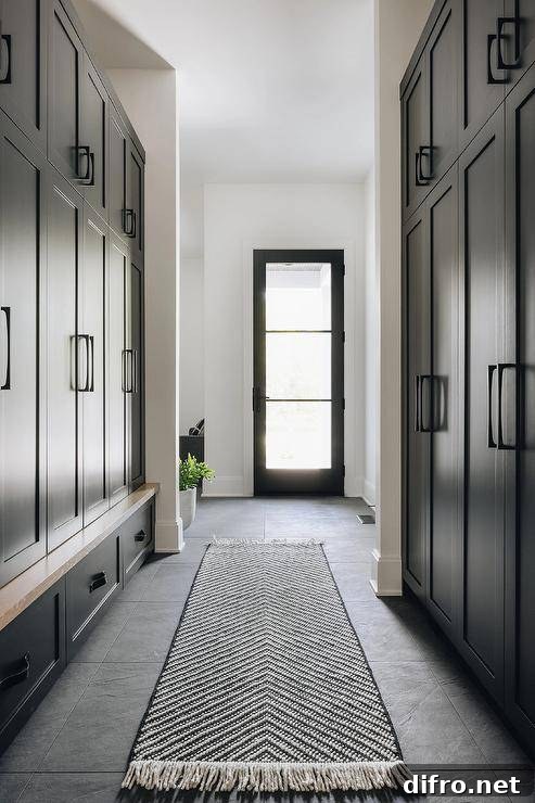 A black chevron runner sits on black floor tiles in a black galley-style mudroom between facing closed black lockers finished with matte black hardware.