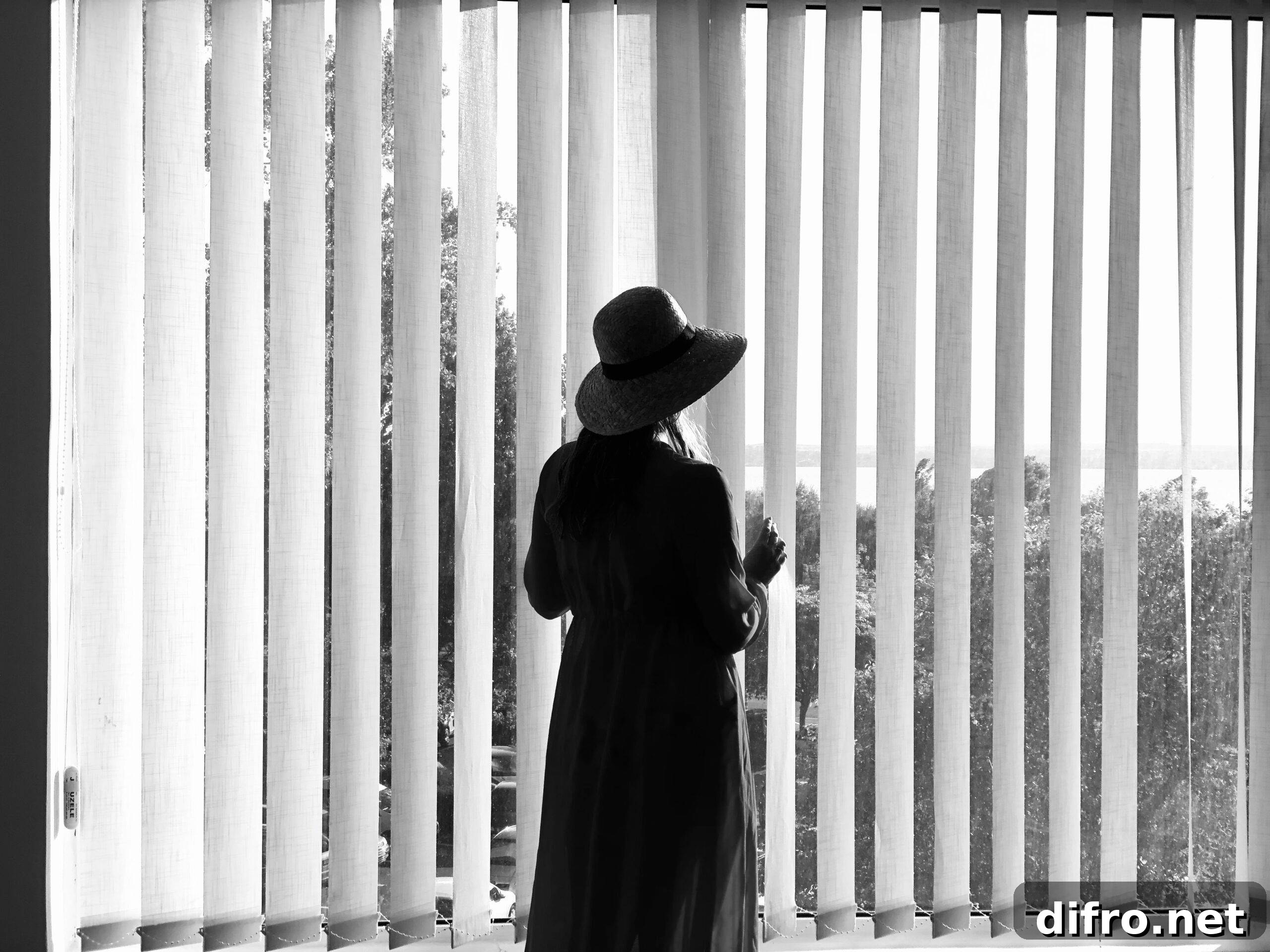 black and white photo of a woman standing in front of a window with vertical blinds