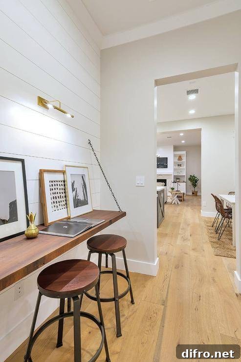 Cottage style workspace with a shiplap wall and wooden wall-mounted desk with framed wall art and round stools.