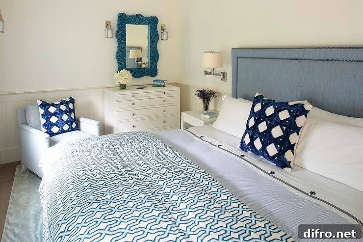 Bedroom features a blue coral mirror over a tall white dresser, a blue headboard with blue trellis pillows and a light blue accent chair.