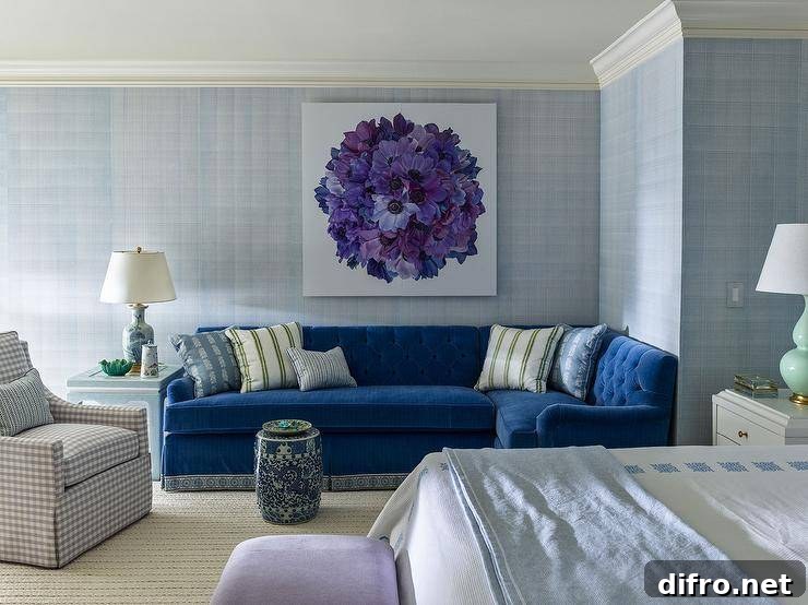 Bedroom features a blue velvet tufted sectional under purple floral art, a blue chinoiserie end table lit by a blue lamp and a gray gingham chair.