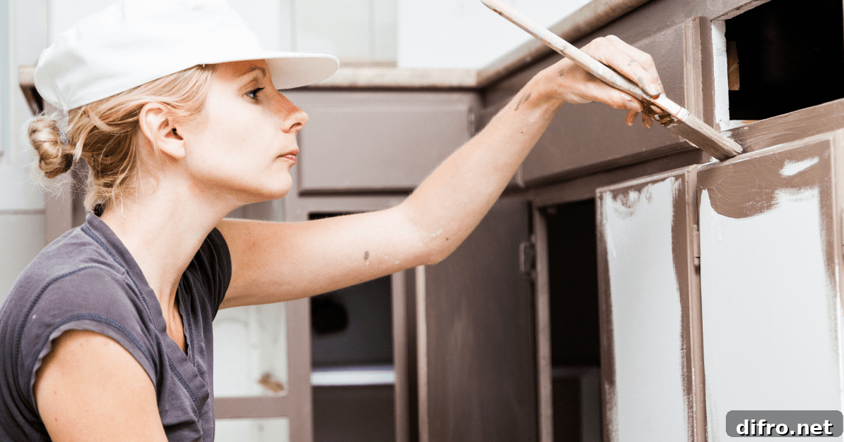 Closeup of woman holding paint brush and painting kitchen cabinets.