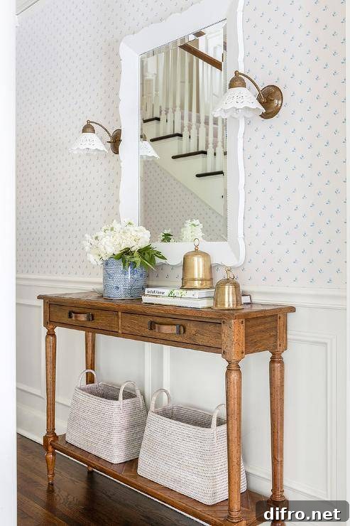 Brass sconces are mounted to a white and blue wallpapered wall lined with white wainscoting