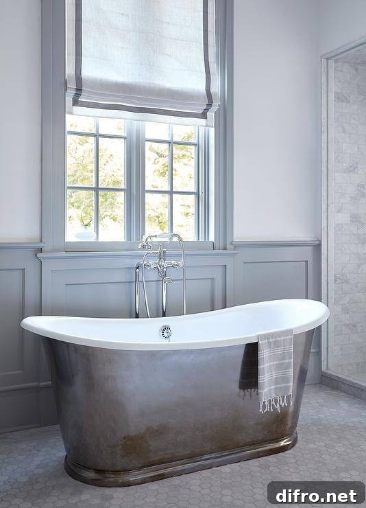 Master bathroom features a modern cast iron tub on marble hexagon floor tiles and gray wainscoting.