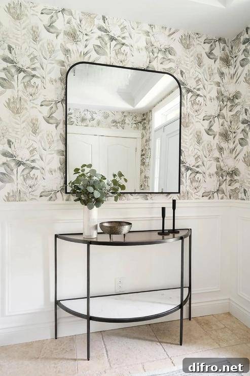 An arch mirror mounted on floral wallpaper over a half-moon console table on wainscoting.