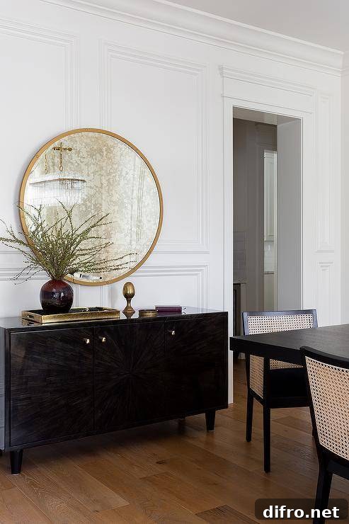 A round gold mirror is mounted on wainscoting over a dark brown buffet cabinet.