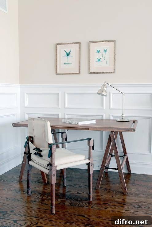 A vintage fabric and wood chair sits at a vintage trestle desk on double wainscoting.