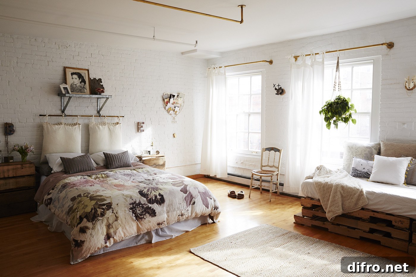 Studio apartment with bed, exposed white brick walls, and a couch made of wooden pallets.