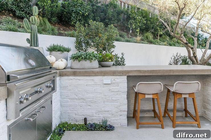 Low back gray rattan barstools sit beneath a concrete countertop accenting a l-shaped outdoor kitchen finished with a stainless steel barbecue.