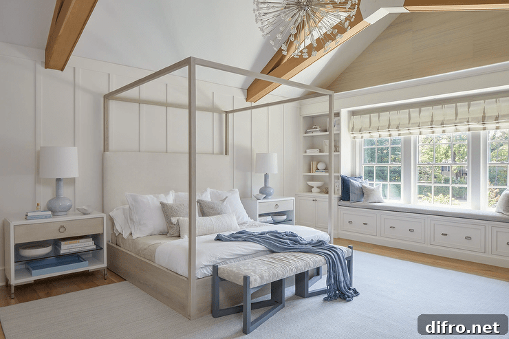 Blue gourd lamps sits atop white and gray nightstands placed against a board and batten wall on either side of a gray oak canopy bed draped with throw blanket. A blue bench sits at the foot of the bed on a light gray rug. A gray roman shade hangs over a long built-in storage bench flanked by built-in bookcases.