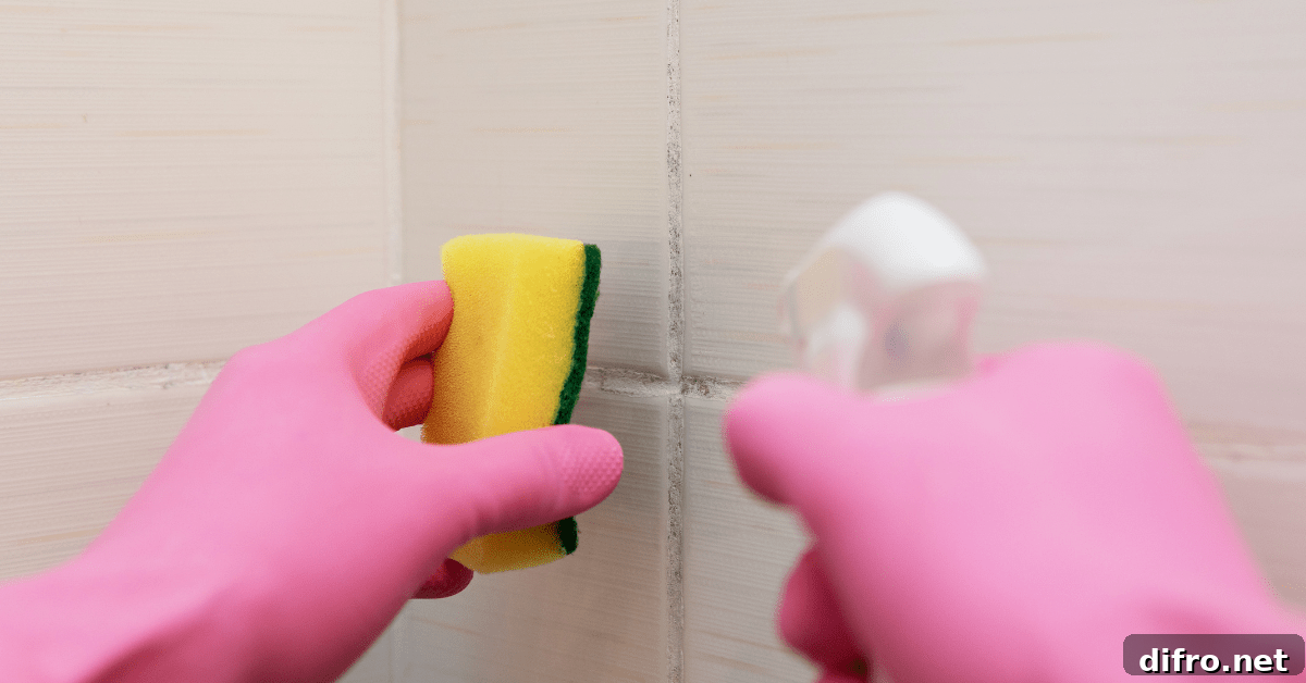 Closeup of someone's hands in pink gloves cleaning tile grout with sponge and spray bottle.