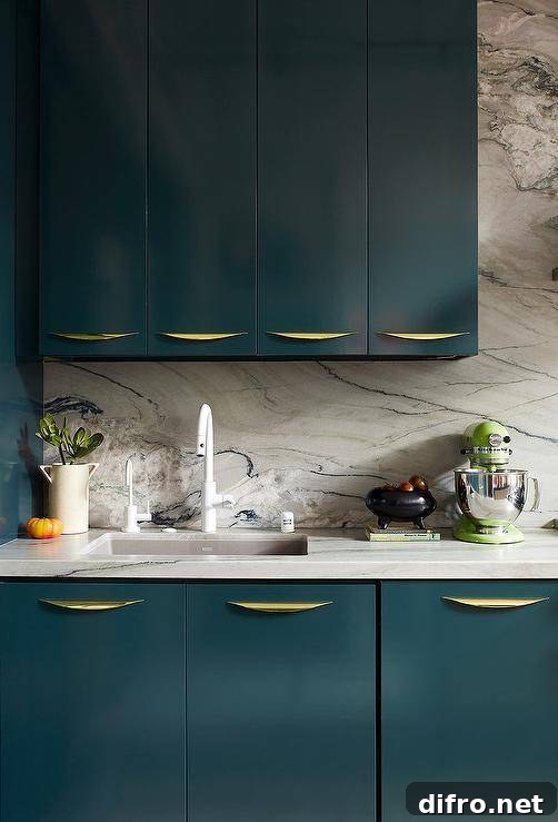 A modern white gooseneck faucet mounted to a honed marble countertop over peacock blue flat front cabinets with curved brass pulls.