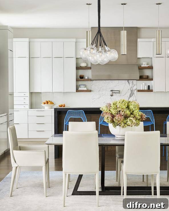 Modern kitchen design features off white leather chairs at a gray marble and black metal dining table lit by modern light bulbs chandelier and white cabinets with nickel pulls.