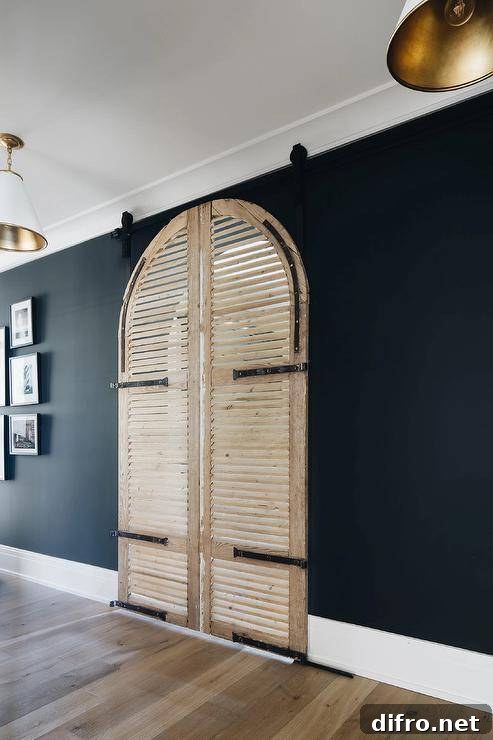 Black mudroom walls contrast stunning arched louvered doors on rails.