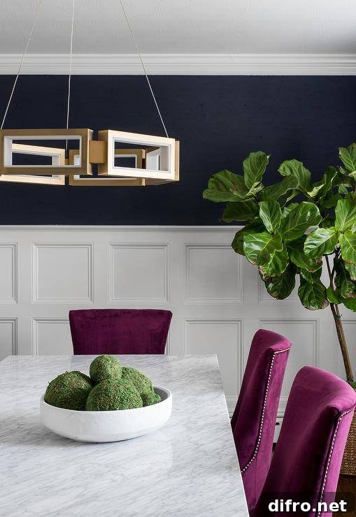 Fuchsia dining chairs and a marble and brass dining table takes notice with its classic materials and stunning bold colors. Navy blue walls combined with white wainscoting trim bring this dining room to life with accents like a fiddle leaf fog plant and a brass geometric pendant.