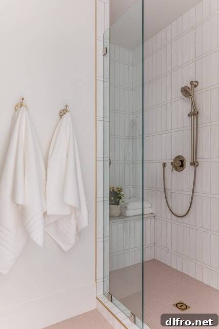 Shower features pink floor tiles, white vertical stacked shower tiles with a satin nickel shower kit, a built in shower bench and a glass partition.