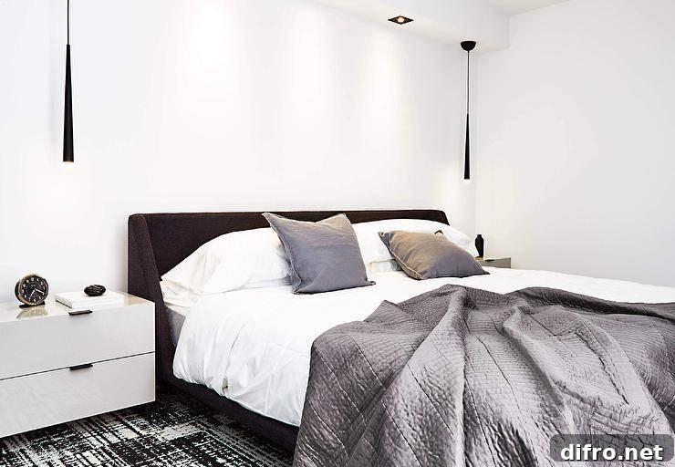 Gray bedding accents a black wingback bed placed on a black and white rug, paired with white lacquer nightstands and black hanging lights.
