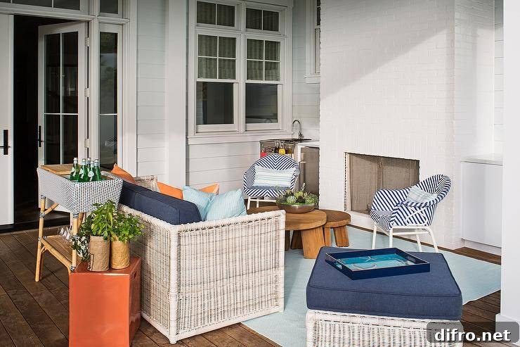 Covered patio featuring a bar sink beside a white brick fireplace furnished with blue herringbone outdoor chairs, nesting coffee tables and white wicker sofa seating.