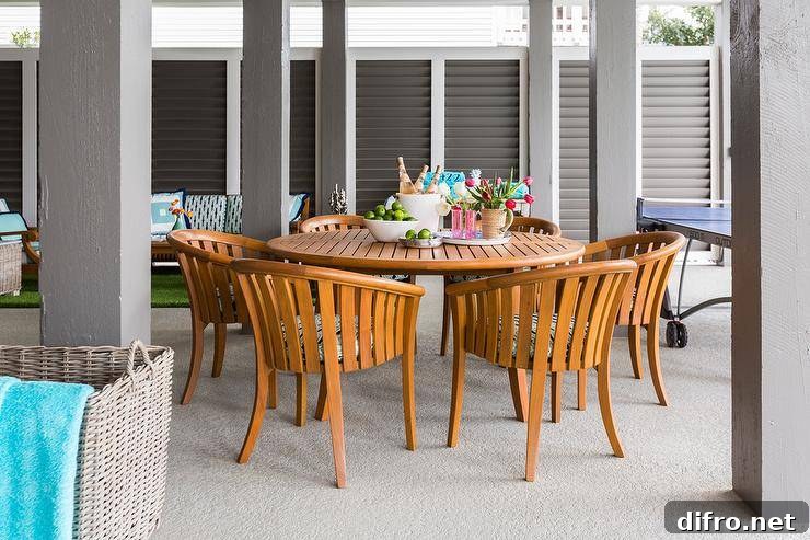 Contemporary covered patio furnished with a round teak dining table and curved teak chairs displaying a summer themed tablescape.