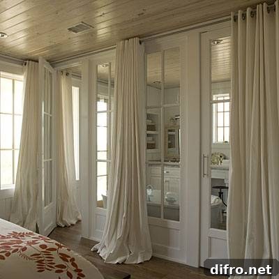 En suite bathroom design features wall of glass doors covered in floor to ceiling ivory grommet drapes.