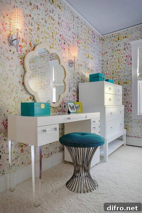 Chic teen girl's bedroom features walls clad in Kandy Brit Pop Wallpaper lined with a white vanity adorned with lucite pulls and lucite legs paired with a turquoise Greek key stool under a cream scalloped mirror, Made Goods Fiona Mirror, next to a Bungalow 5 Pandora Tall 4 Drawer.