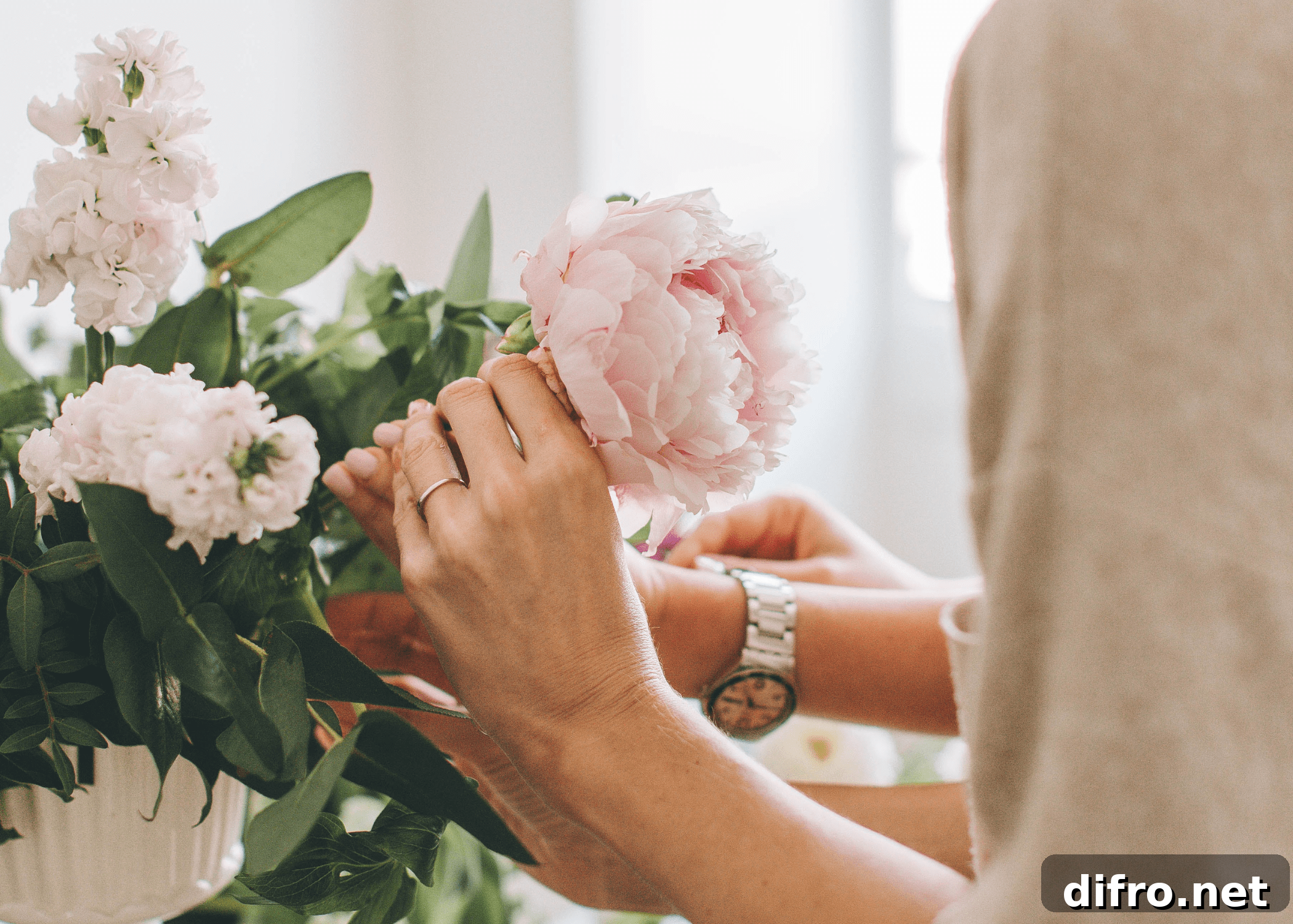 woman placing a pink peony in a flower arrangement