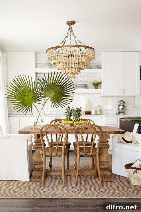 Beige beaded chandelier over a small reclaimed wood dining table with white slipcovered and bistro chairs on a jute rug, balancing warm and cool tones.