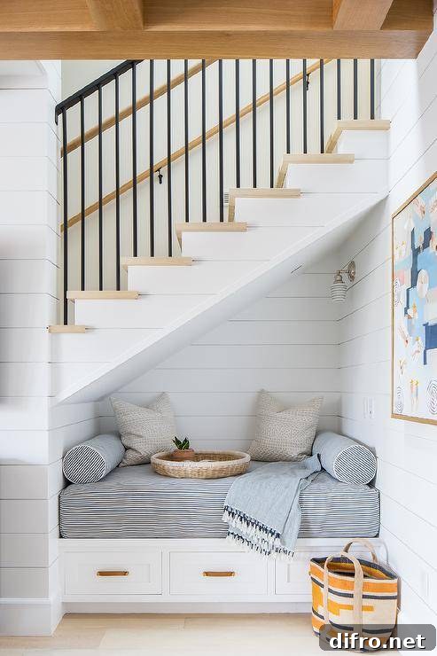Beneath a staircase boasting blond wood treads, a white shiplap reading nook is fitted with a white built-in bench.
